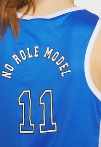 Modrý dres s bílým lemem, na zadní straně s textem "NO ROLE MODEL" a číslem "11" vytištěným černým obrysem. Texturovaná tkanina.