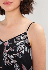 Top senza maniche nero con motivo floreale, caratterizzato da scollatura a V, spalline sottili e motivi di foglie multicolori in tonalità di rosa e argento. Tessuto morbido al tatto.