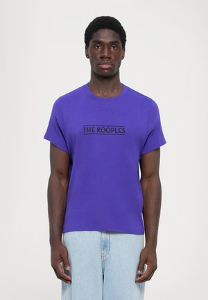 Vijolična bombažna majica s kratkimi rokavi in okroglo izrezo, ki ima črni logotip "THE KOOPLES" na prsih. Oblika je sproščena.