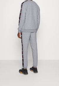 Grijze sweatshirt en broek set van zacht materiaal. Bevat een zwarte en rode logo-printstreep langs de zijkanten. Inclusief ribgebreide manchetten en tailleband.