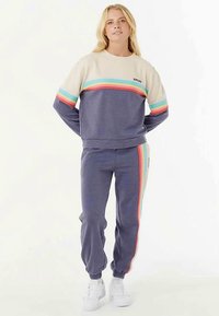 Sweatshirt en joggingbroek set in marineblauw en crème, met horizontale meerkleurige strepen. Zachte textuur met geribbelde manchetten en tailleband.