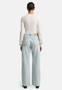 Top lungo beige chiaro a maniche lunghe con scollatura rotonda, abbinato a jeans a vita alta e gamba larga di colore azzurro chiaro, con un'etichetta in pelle sul retro.
