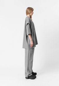 Blusa gris de gran tamaño con mangas cortas y un bolsillo de parche, combinada con pantalones grises a juego. Los pantalones cuentan con cremalleras en los tobillos. Tejido texturizado.