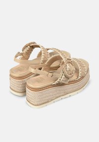 Sandali piatti beige con cinturini intrecciati e rosellina decorativa. Presentano una suola piatta in tessuto simile al juta e una soletta imbottita.