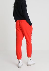 Punaiset juoksuhousut, joissa on kapeneva leikkaus, joustava vyötärö ja resorit. Yhdistettynä valkoisiin lenkkitossuihin ja mustavalkoisiin raidallisiin sukkiin.