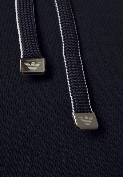 Tissu navy avec une surface texturée, comprenant deux cordes tissées sombres avec des accents en matériel argenté et un logo embossé aux extrémités.