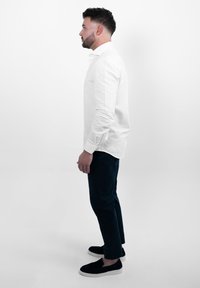 Witte blouse met lange mouwen en een knoopsluiting, gecombineerd met donkergroene broek en zwarte instappers. Eenvoudig ontwerp met een strakke silhouet.
