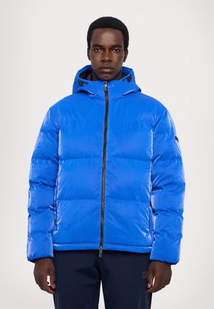 Giacca a vento blu con texture lucida, chiusura a zip, cappuccio regolabile e logo discreto sul davanti. Presenta polsini elasticizzati.