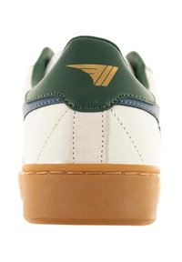 Zapatilla de cuero blanca con acentos verdes, detalles azules, logo dorado cerca del talón y una suela de goma marrón. Textura suave con detalles de costura.