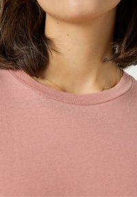 Jasnoróżowy bawełniany T-shirt z okrągłym dekoltem i krótkimi rękawami, o gładkiej fakturze i prostym, nieozdobionym wzornictwie.