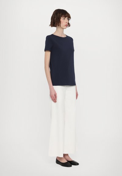 Haut à manches courtes marine associé à un pantalon large blanc et des ballerines noires. Tissu lisse, design minimaliste et silhouette ajustée.
