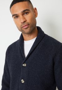 Cardigan lavorato a maglia blu navy scuro con collo sciallato, caratterizzato da una trama a coste e tre bottoni marrone chiaro con centri scuri.