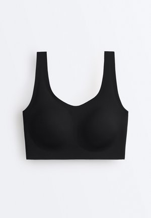 Soutien-gorge sans fil noir avec bretelles larges, bonnets sans coutures, et tissu lisse et élastique sur fond blanc uni.