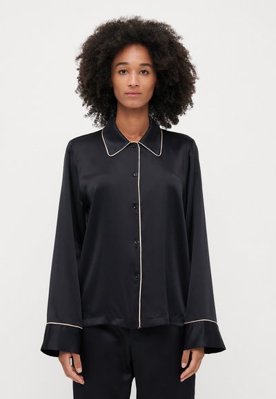 Sort satin pyjamashirt med spids krave, knaplukning foran og kontrastfarvet lys piping langs kraven og ærmerne. Lange ærmer.