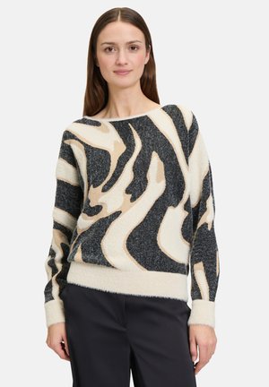 Pull en tricot avec un motif animal ondulé en noir, beige et crème. Tissu doux et texturé avec un col bateau et des poignets côtelés.