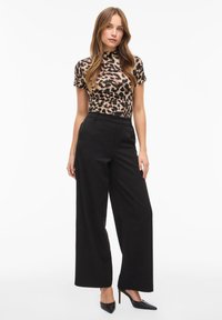 Top de manga corta con estampado de leopardo combinado con pantalones negros de tiro alto y pierna ancha, y tacones negros puntiagudos. Tejido liso y corte entallado.