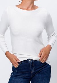 Top lungo a maniche lunghe bianco a coste con scollatura a barca, design aderente e tessuto testurizzato, abbinato a jeans blu scuro.