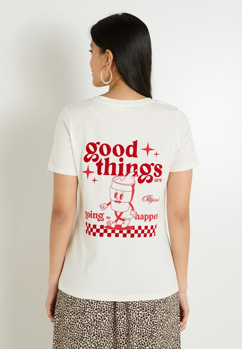 T-shirt couleur crème avec un texte graphique rouge et un personnage de dessin animé au dos, accompagné d'un motif à carreaux en bas.