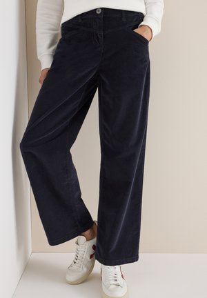 Pantalons larges en velours côtelé bleu marine avec poches avant et fermeture à bouton, assortis à des baskets blanches, sur un fond neutre.