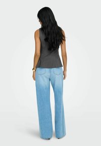 Grå peplum vest med en skræddersyet pasform, parret med lyseblå bredbenede denimjeans. Glat stoftekstur og minimal detaljering.