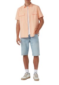 Licht perzikkleurig overhemd met korte mouwen en twee borstzakken, gecombineerd met lichtblauwe denim shorts tot de knie en witte sneakers.