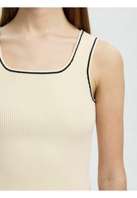 Ribbed top na ramiączkach w kremowym kolorze z czarnym wykończeniem wzdłuż kwadratowego dekoltu i otworów na ramiona. Materiał ma miękką teksturę, dopasowany krój.