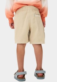 Beiga bomullsshorts med elastisk midja, sidofickor och en bakficka. Bärs med ljusblå sandaler med ett remdesign.
