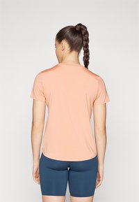 Camiseta deportiva de manga corta color durazno claro con escote redondo, combinada con pantalones cortos azul oscuro. Tejido suave con un diseño ajustado.