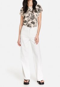 Top beige con estampado floral combinado con pantalones anchos blancos y sandalias de plataforma negras. El top tiene un corte holgado y mangas cortas.