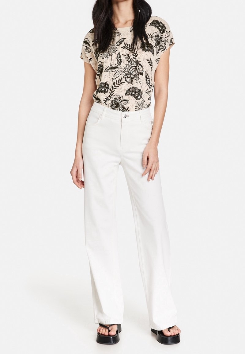 Top beige con estampado floral combinado con pantalones anchos blancos y sandalias de plataforma negras. El top tiene un corte holgado y mangas cortas.