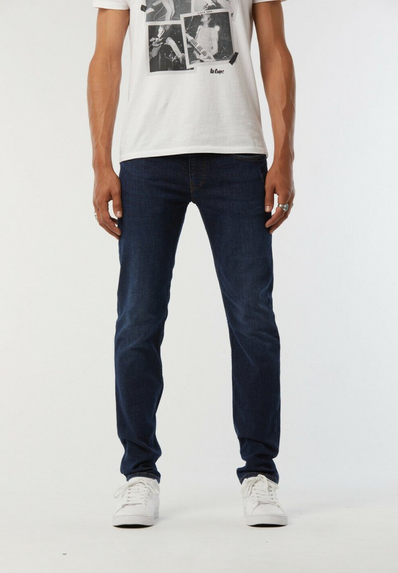 Jean en denim bleu foncé avec une coupe slim, doté d'un design classique à cinq poches. Associé à un t-shirt graphique blanc et des baskets blanches.
