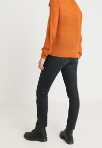 Orange stickad tröja med ett strukturerat mönster, kombinerad med svarta slim-fit jeans och svarta snörstövlar. Visar en avslappnad outfit.