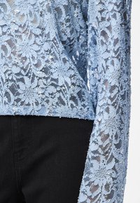 Light blue lace top featuring floral patterns, sequins, and transparent texture; paired with black fabric at the hem and sleeve.