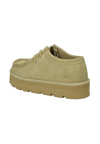 Scarpe lacci beige in suede con suola in gomma, dotate di colletto imbottito e dettagli di cucitura, etichettate "Wallabees" sul lato.
