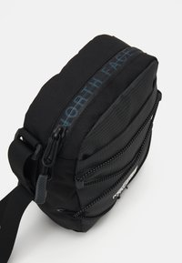Borsa a spalla nera con tasche multiple con zip, tessuto testurizzato e tracolla regolabile. Presenta il marchio "NORTH FACE" in blu.