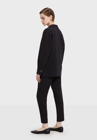 Zwarte hoge hals langemouwen shirt gecombineerd met slanke zwarte broek, met een gladde textuur en minimalistisch ontwerp. Zwarte flats maken de look compleet.