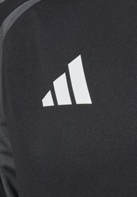 Schwarzes Sportshirt mit grauen Akzenten, das auf der oberen linken Seite ein auffälliges weißes Drei-Streifen-Logo aufweist. Glattes, strukturiertes Material.