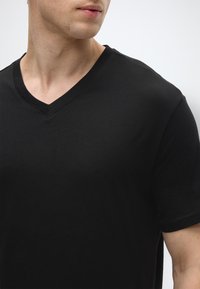 Μαύρο βαμβακερό μπλουζάκι με V-λαιμόκοψη, κοντά μανίκια και απαλή υφή, με καθαρές γραμμές και απλό, λιτό στυλ.