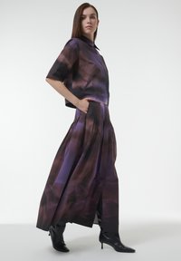 Two-piece outfit with a cropped, short-sleeve blouse and a long, pleated skirt. Features a purple and dark brown abstract pattern, made of lightweight fabric.