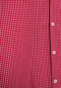 Czerwona tkanina z białym wzorem w kratkę, z pionowym szwem i trzema widocznymi białymi guzikami po prawej stronie.