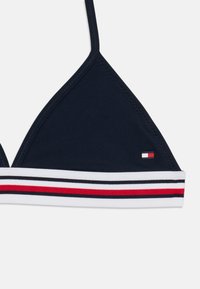 Marineblå trekantet bikini-top med en hvid, rød og sort stribet kant. Har et brandet logo i en lille lap på den ene side.