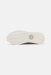 Suola della scarpa in gomma beige, con un motivo testurizzato a puntini per una presa migliore, dotata di un design segmentato e un dettaglio di branding circolare.