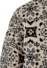 Fleece-kangasvaate, jossa on kerma-alue mustilla monimutkaisilla kukka- ja geometrisia kuvioita. Pehmeä pinta ja lämmin ulkonäkö.