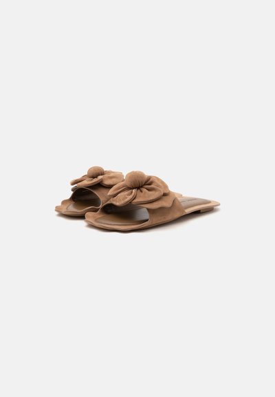 Paire de sandales plates ouvertes marron avec de grands nœuds en tissu sur le dessus, présentée sur un fond clair uni.