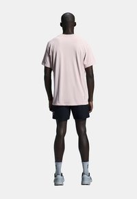 Lys rosa kortærmet t-shirt, sorte shorts, grå sportssko og hvide sokker. Casual pasform, glat stof, uden synlige mønstre eller grafik.
