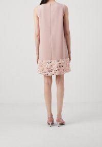 Robe sans manches en tissu rose doux, dotée d'un ourlet en sequins et franges. Fermeture éclair au dos, coupe droite, longueur genou.
