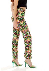 Floral-patterned trousers with a fitted waist, made from lightweight fabric. Colors include green, pink, and yellow. Paired with green high heels.