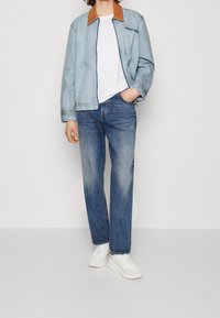 Ljusblå denimjacka med en brun läderkrage, ihop med blå raka jeans och vita sneakers. Avslappnad, ledig passform.