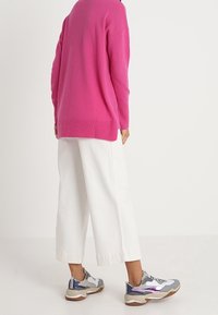 Rosa oversized tröja, vita vida byxor och grå sneakers med lila detaljer. Mjuk textur och avslappnad passform hela vägen igenom.