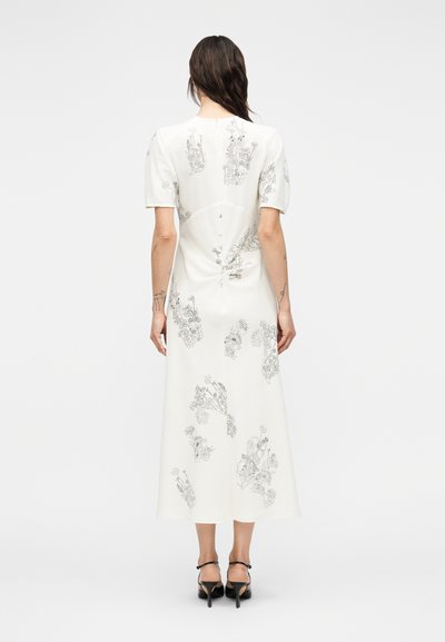 Λευκό midi φόρεμα με κοντά φουσκωτά μανίκια, διακοσμημένο με μαύρα λουλουδάτα σχέδια γραμμής. Λείο ύφασμα με εφαρμογή που τονίζει τη σιλουέτα και λεπτομέρειες κουμπιών στο πίσω μέρος.